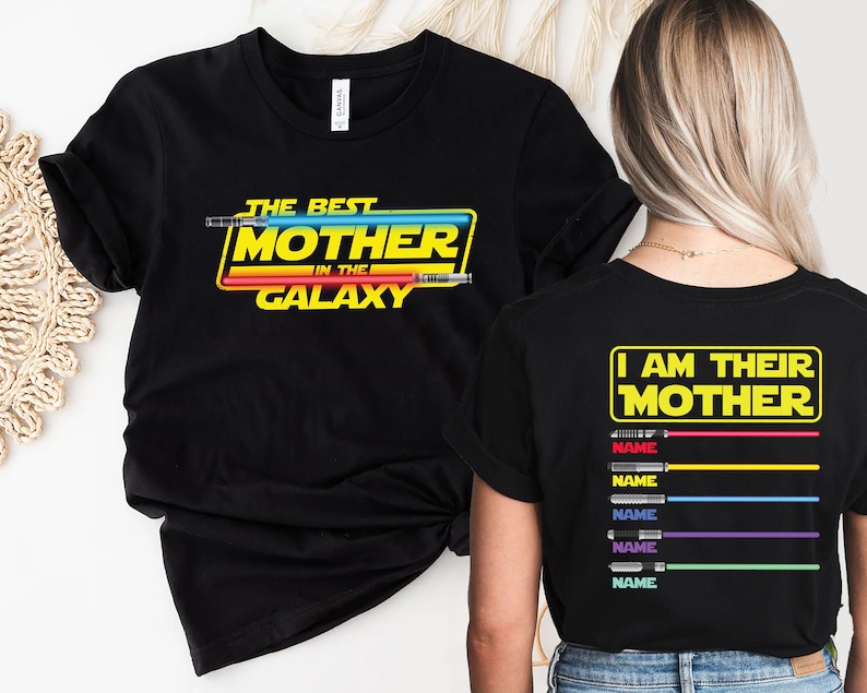 Puede incluir: Dos camisetas negras con un dise&ntilde;o de tem&aacute;tica de Star Wars. La camiseta delantera dice "The Best Mother in the Galaxy" con un gr&aacute;fico de sable de luz. La camiseta trasera dice "I Am Their Mother" con un gr&aacute;fico de sable de luz y espacio para nombres.