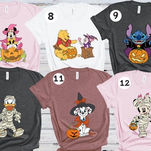 Op de afbeelding: Zes verschillende T-shirts met verschillende Disney-figuren in Halloween-kostuums. De shirts zijn roze, wit, grijs, roodbruin en lichtroze. De figuren zijn Mickey Mouse, Winnie de Poeh, Stitch, Donald Duck, een dalmati&euml;r en Minnie Mouse.