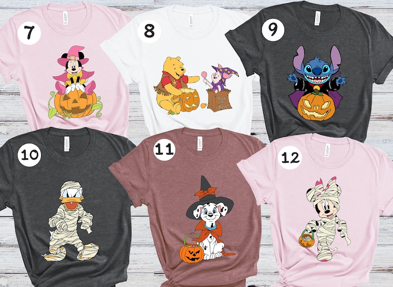 Op de afbeelding: Zes verschillende T-shirts met verschillende Disney-figuren in Halloween-kostuums. De shirts zijn roze, wit, grijs, roodbruin en lichtroze. De figuren zijn Mickey Mouse, Winnie de Poeh, Stitch, Donald Duck, een dalmati&euml;r en Minnie Mouse.