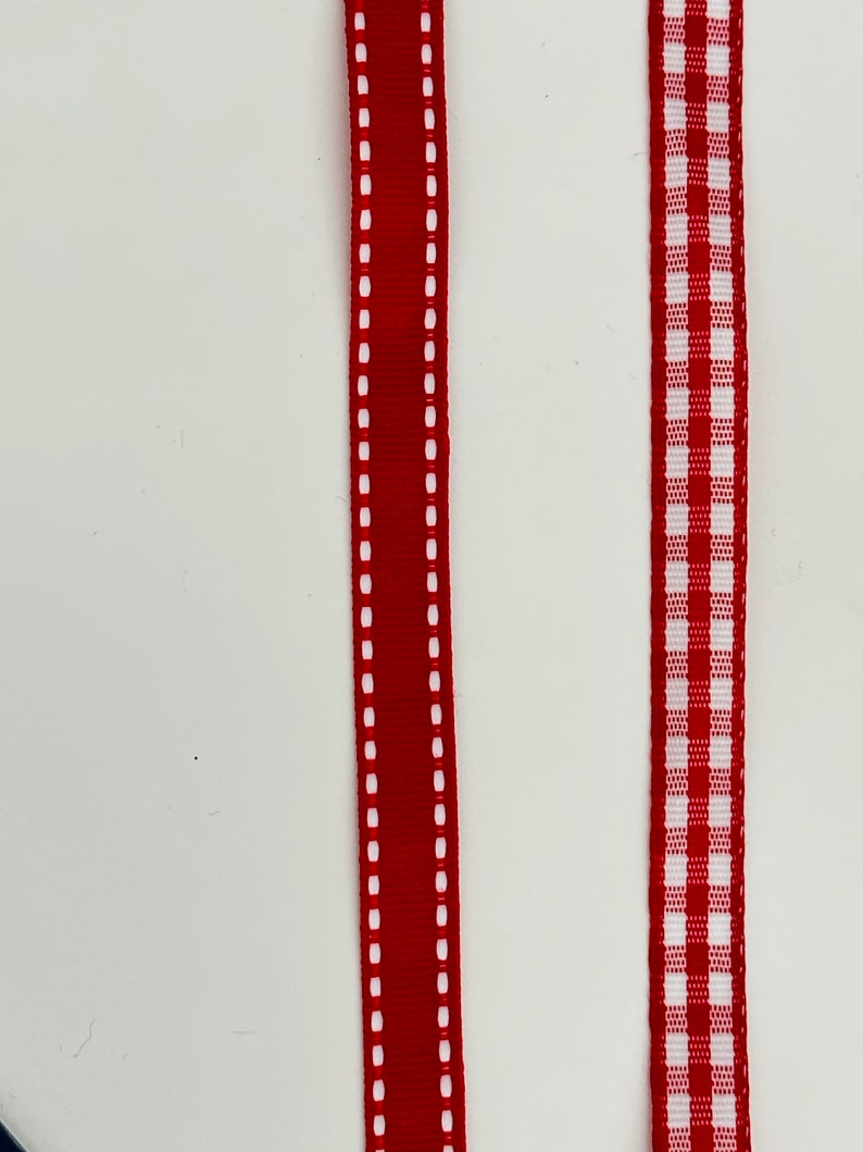 May include: Two red ribbons with white stitching. One ribbon has a solid red center with white stitching on the edges. The other ribbon has a white and red checkered pattern.