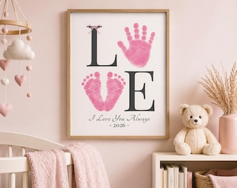 May include: Framed print with the word "LOVE" in black letters, featuring a pink handprint, footprint, and the text "I Love You Always - 2026". The print is in a wooden frame, displayed in a nursery setting.