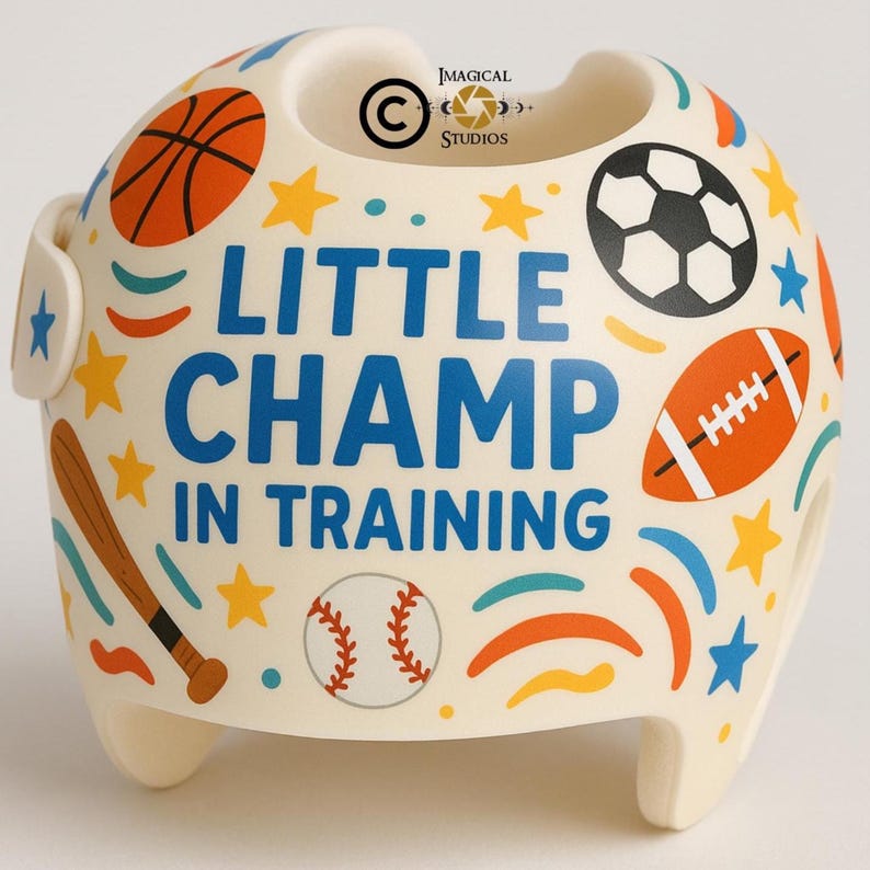Puede incluir: Casco infantil de color crema decorado con gr&aacute;ficos tem&aacute;ticos deportivos, incluyendo una pelota de baloncesto, un bal&oacute;n de f&uacute;tbol y un bal&oacute;n de f&uacute;tbol americano. El texto "LITTLE CHAMP IN TRAINING" se muestra en azul. Estrellas y un bate de b&eacute;isbol completan el dise&ntilde;o.