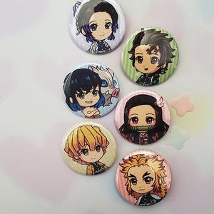May include: Six round button badges featuring characters from the anime Demon Slayer. The characters are depicted in a chibi style with colourful backgrounds.