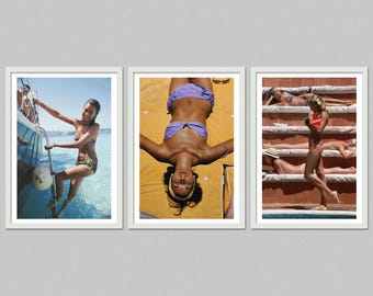 May include: A set of three framed prints featuring beach scenes. One print shows a woman climbing a boat ladder. Another shows a woman sunbathing. The third print shows several people sunbathing near a pool.