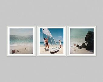 May include: Set of three framed beach prints. The first print shows a beach scene with ocean waves. The second print features a man with a sailboat on the beach. The third print shows a beach with rocks and people.