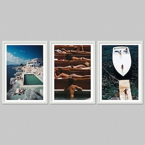 May include: A set of three framed prints. One shows a coastal pool scene with a white building and blue sky. Another depicts people sunbathing on tiered steps. The third features a boat and a wooden jetty.