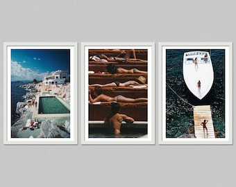 May include: Set of three framed prints. One shows a coastal pool scene with a white building and blue sky. Another depicts people sunbathing on tiered steps. The third features a boat and a wooden dock.
