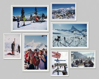 May include: A collection of framed vintage photographs depicting scenes of skiing and winter activities. The images show people on skis, a helicopter, mountain landscapes, and outdoor gatherings. The frames are white, and the background is a neutral gray.