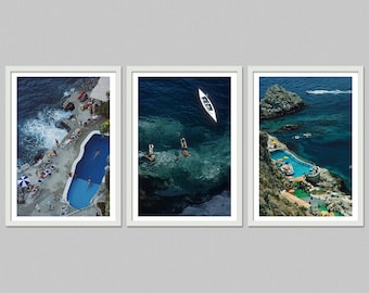 May include: Set of three framed art prints featuring aerial views of coastal scenes. One shows a pool, another swimmers and a boat in the sea, and the third a pool and rocky coastline. The images have a vintage, travel-inspired aesthetic.