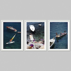 May include: A set of three framed prints featuring scenes of boats and people on the water. One print shows a sailboat and a motorboat. Another shows a white boat near a dock with people sunbathing. The third print shows a motorboat with people.