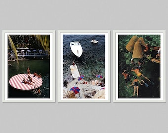 May include: Set of three framed art prints featuring vintage-style beach scenes. One print shows people on a striped floating platform, another a boat near a dock, and the third people snorkeling.