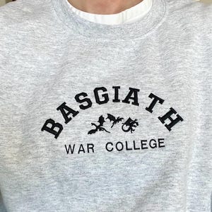 May include: A gray sweatshirt with a black embroidered design that reads "BASGIATH WAR COLLEGE" with three black dragon silhouettes.