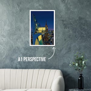 Op de afbeelding: Een ingelijste print met een gestileerde stadsgezicht bij zonsondergang. Het kunstwerk toont een moderne wolkenkrabber met het Avengers-logo en het Empire State Building. De tekst "A1 PERSPECTIVE" staat eronder.
