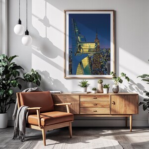 Op de afbeelding: Een ingelijste kunstdruk met een stadsgezicht met het Avengers-logo. Het kunstwerk wordt tentoongesteld boven een houten kast met een leren fauteuil en planten. De print heeft een houten lijst en toont een nachtsc&egrave;ne met verlichte gebouwen.