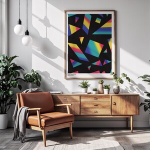 May include: A framed abstract art print with a black background and colorful geometric shapes in shades of yellow, blue, and pink. The print hangs above a wooden mid-century modern style cabinet and a brown leather armchair.