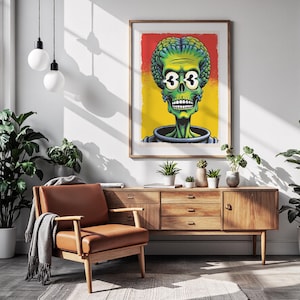 Puede incluir: Una impresión artística enmarcada que presenta un alienígena verde con el número "33" en sus ojos, sobre un fondo rojo y amarillo. La obra de arte se exhibe en una sala de estar con un sillón de cuero marrón y un mueble de madera.