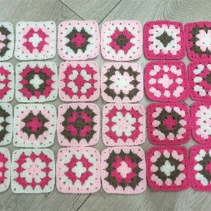 Puede incluir: Una manta de ganchillo hecha de cuadrados en rosa, blanco y marrón. Los cuadrados están dispuestos en un patrón de cuadrícula.