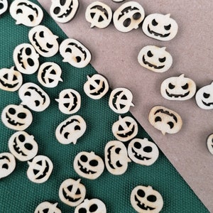 Op de afbeelding: Een verzameling houten pompoenvormen met uitgesneden jack-o'-lantern gezichten. De vormen zijn verspreid over een groen en bruin oppervlak.