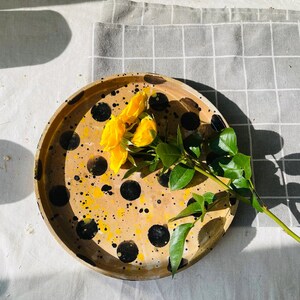 Op de afbeelding: Een ronde dienblad met zwarte en gele stippen. Een boeket gele rozen ligt op het dienblad.