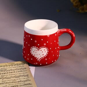 May include: Red ceramic mug with white polka dots and a white heart with white polka dots. The heart has a stitched outline.
