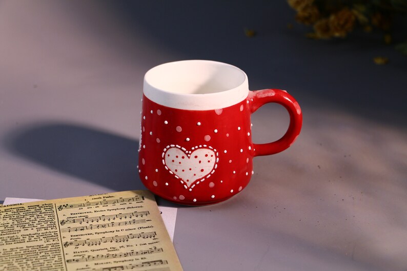 May include: Red ceramic mug with white polka dots and a white heart with white polka dots. The heart has a stitched outline.