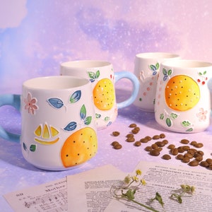 May include: Four white ceramic mugs with colorful painted designs. Each mug features a different design with a yellow citrus fruit, flowers, and leaves. The mugs have blue handles.