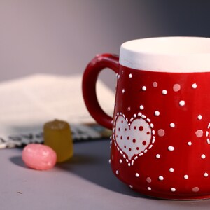 May include: Red ceramic mug with white polka dots and two white hearts with white polka dots. The hearts have white stitching around the edges.