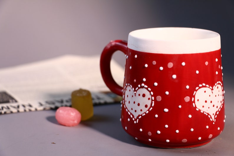 May include: Red ceramic mug with white polka dots and two white hearts with white polka dots. The hearts have white stitching around the edges.