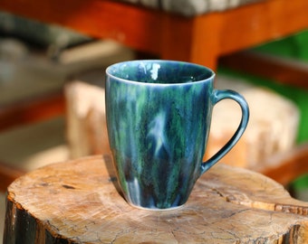 May include: A blue and green ceramic mug with a unique marbled glaze. The mug has a rounded body and a handle.