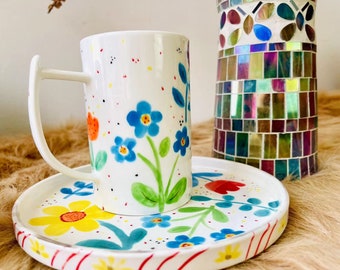 Juego de taza y plato de cerámica pintados a mano con diseños florales.