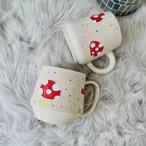 Close-up of a hand-painted ceramic mug with an adorable red mushroom illustration.