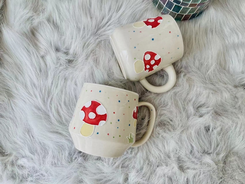 Close-up of a hand-painted ceramic mug with an adorable red mushroom illustration.