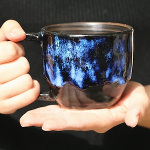 May include: A black ceramic mug with a blue and white glaze. The mug has a rounded shape and a handle.