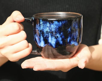 May include: A black ceramic mug with a blue and white glaze. The mug has a rounded shape and a handle.