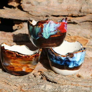 May include: Three ceramic bowls with a rustic, hand-crafted look. The bowls are stacked on top of each other and have a variety of colours, including brown, blue, and green.