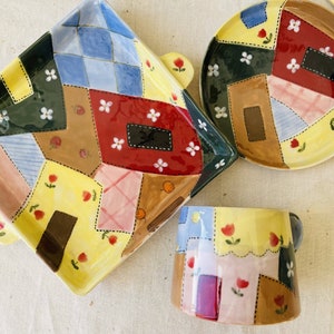Pode incluir: Um conjunto de três pratos de cerâmica com um design de patchwork. Os pratos são amarelos, vermelhos, azuis, verdes, castanhos e cor-de-rosa com flores brancas e detalhes pretos. Os pratos são perfeitos para servir petiscos, entradas ou sobremesas.