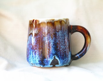 May include: A blue and brown ceramic mug with a textured glaze. The mug has a rounded body and a handle.