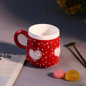 Unique handmade red ceramic mug featuring playful heart patterns.