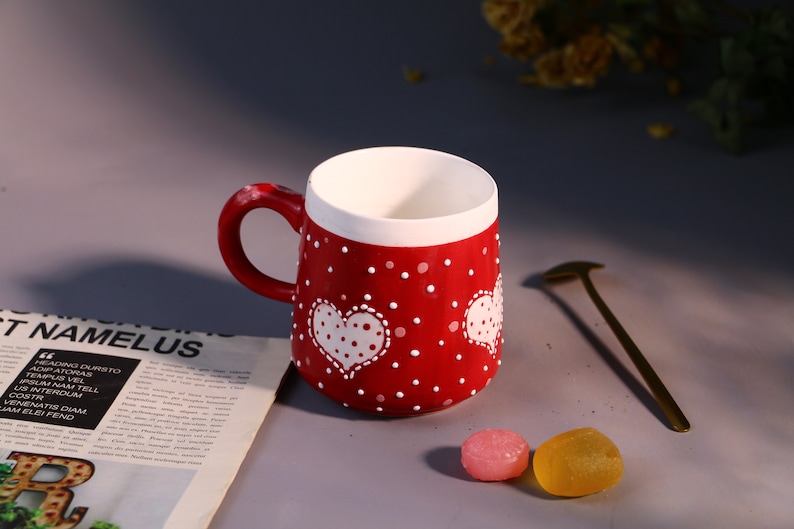 Unique handmade red ceramic mug featuring playful heart patterns.