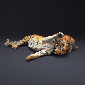May include: Two orange and black striped tigers playing together. The larger tiger is lying on its back with its paws in the air, while the smaller tiger is standing on its hind legs and playfully biting the larger tiger's neck.