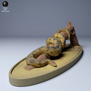 Op de afbeelding: Een geel en zwart anaconda-slangenbeeldje dat om een ​​bruine boomtak gekruld is. De slang staat op een ovale basis van beige met een bruine rand.