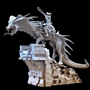 Puede incluir: Una figura miniatura pintada de blanco de una guerrera montando un dragón. El dragón está de pie sobre una base de piedra con una pared rota. La guerrera sostiene una espada y lleva un casco.