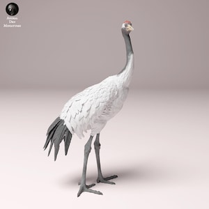 Puede incluir: Una figurita de grúa blanca y gris con una corona roja en la cabeza. La grúa está de pie sobre una superficie blanca.