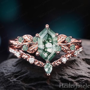 May include: A rose gold ring set with a large, green, patterned gemstone. The set includes a leaf-detailed band and a diamond-set band. The design is elegant and nature-inspired. The text "Heslerfinejewelry" is visible on the bottom right.