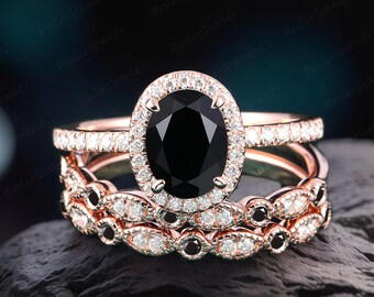 May include: A three-piece rose gold engagement ring set with a black oval center stone and a halo of smaller diamonds. The band is also set with smaller diamonds.