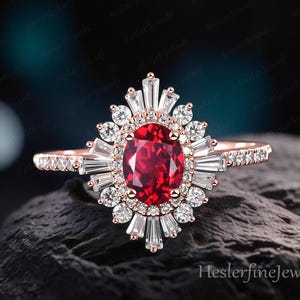 Può includere: Un anello in oro rosa con un grande rubino centrale ovale, circondato da un alone di diamanti rotondi e baguette. Anche la fascia dell'anello è ornata da piccoli diamanti. L'anello è appoggiato su una superficie scura e strutturata.