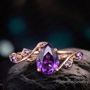 以下が含まれることがあります： 梨型のアメジストの宝石をセットしたローズゴールドの婚約指輪。繊細な葉のデザインで、小さなアメジストのアクセントが施されています。