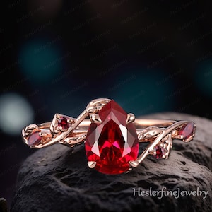 May include: A pear-shaped ruby engagement ring set in rose gold with a delicate leaf design and smaller ruby accents.