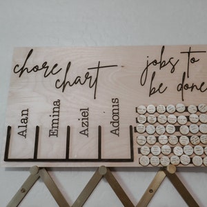 May include: A wooden chore chart with the names Alan, Emina, Aziel, and Adomnis. The chart has a section for "jobs to be done" with a grid of small wooden circles.