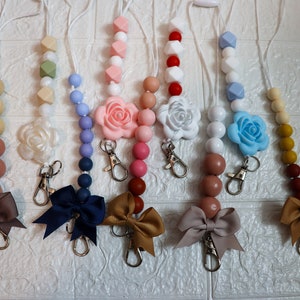 May include: Seven colorful silicone bead necklaces with flower charms and bow accents. Each necklace has a silver key ring attached.